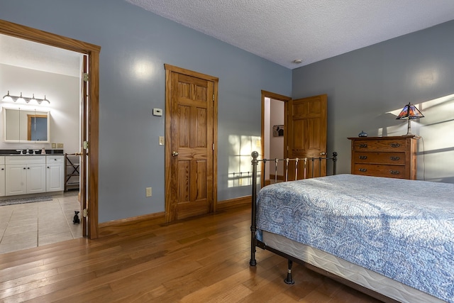 bedroom featuring sink, light hardwood / wood-style floors, a textured ceiling, and ensuite bathroom