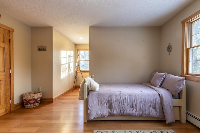 bedroom with light wood-type flooring, a textured ceiling, and a baseboard heating unit