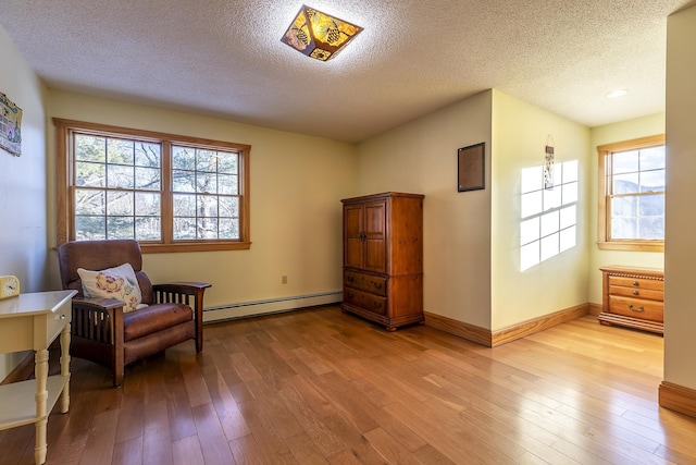 living area featuring a baseboard radiator, light hardwood / wood-style floors, a textured ceiling, and plenty of natural light