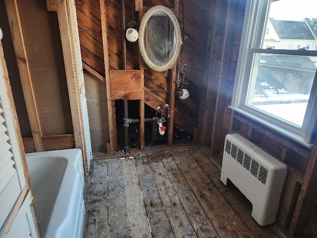 bathroom featuring hardwood / wood-style floors, radiator heating unit, wooden walls, and a tub to relax in