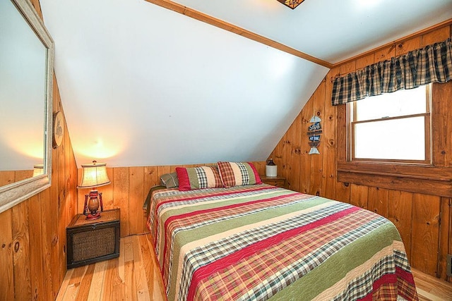 bedroom featuring vaulted ceiling, wooden walls, and light hardwood / wood-style floors