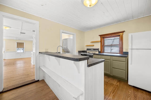 kitchen with range with gas stovetop, white refrigerator, green cabinets, kitchen peninsula, and light wood-type flooring