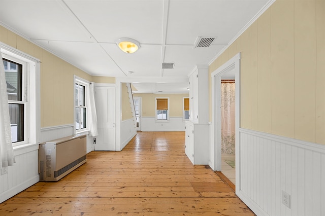 hallway with ornamental molding, heating unit, and light wood-type flooring