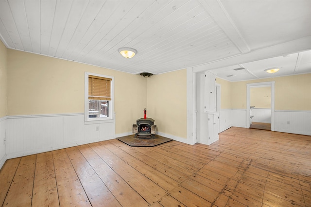 spare room with light wood-type flooring, wooden ceiling, and a wood stove