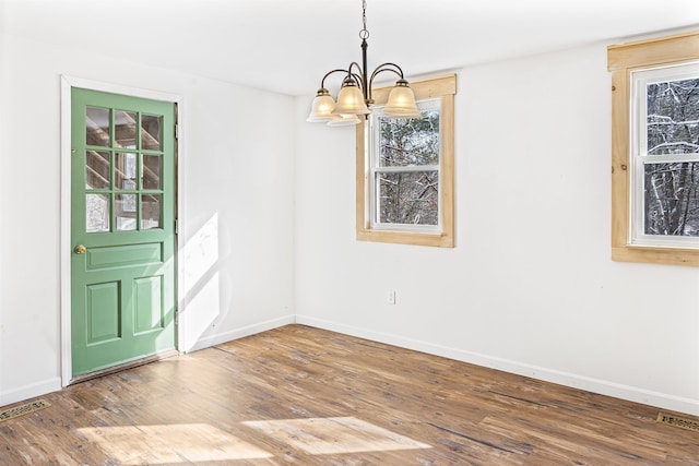 unfurnished dining area featuring a wealth of natural light, hardwood / wood-style floors, and an inviting chandelier