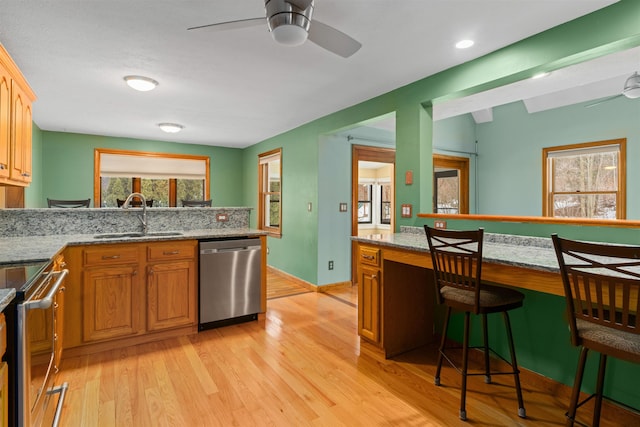 kitchen featuring sink, light wood-type flooring, light stone countertops, and appliances with stainless steel finishes