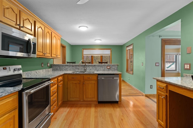 kitchen featuring appliances with stainless steel finishes, sink, kitchen peninsula, light stone countertops, and light wood-type flooring