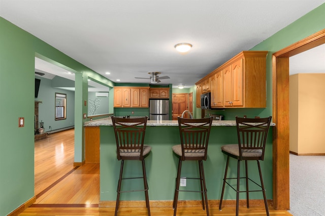 kitchen with light wood-type flooring, a baseboard heating unit, a breakfast bar area, and appliances with stainless steel finishes