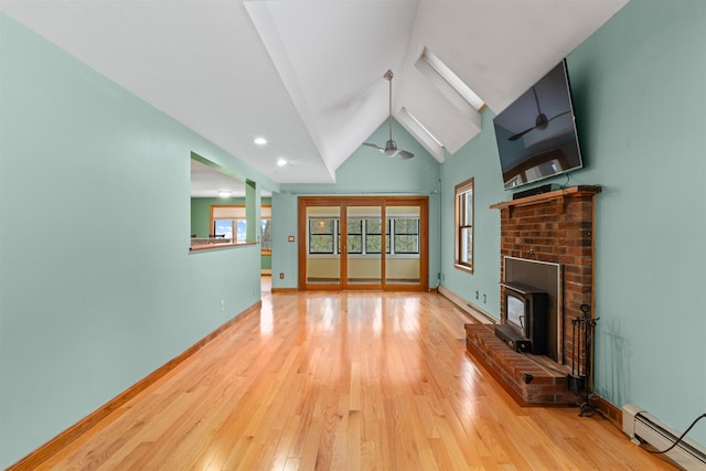 unfurnished living room featuring vaulted ceiling with skylight, light wood-type flooring, a wood stove, and a baseboard heating unit