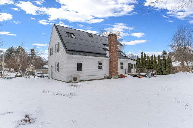 snow covered rear of property with a wooden deck, ac unit, and solar panels