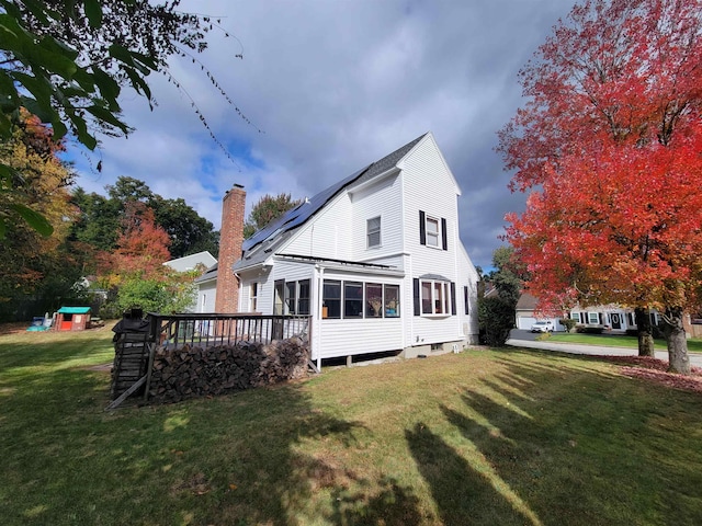 rear view of property featuring a wooden deck, a yard, and solar panels