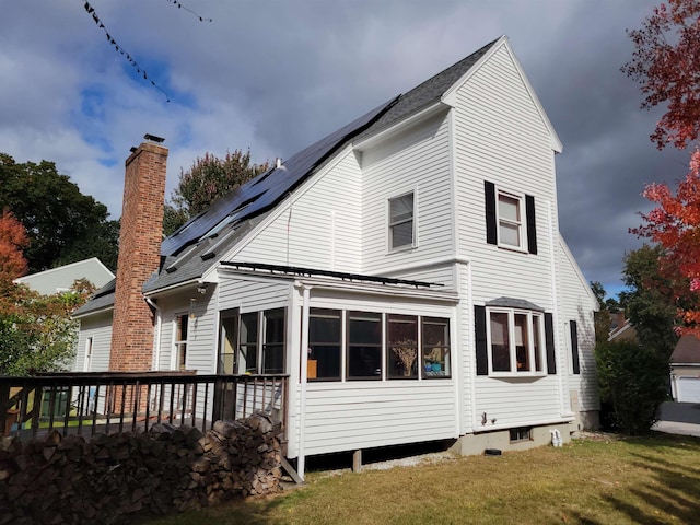 back of house featuring a lawn, a sunroom, and solar panels