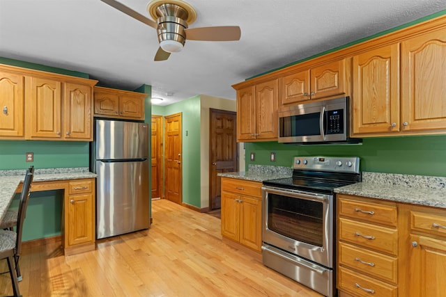 kitchen featuring built in desk, ceiling fan, light hardwood / wood-style floors, stainless steel appliances, and light stone countertops