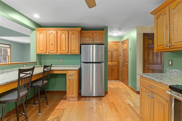 kitchen featuring stainless steel appliances, light stone countertops, light hardwood / wood-style flooring, and built in desk