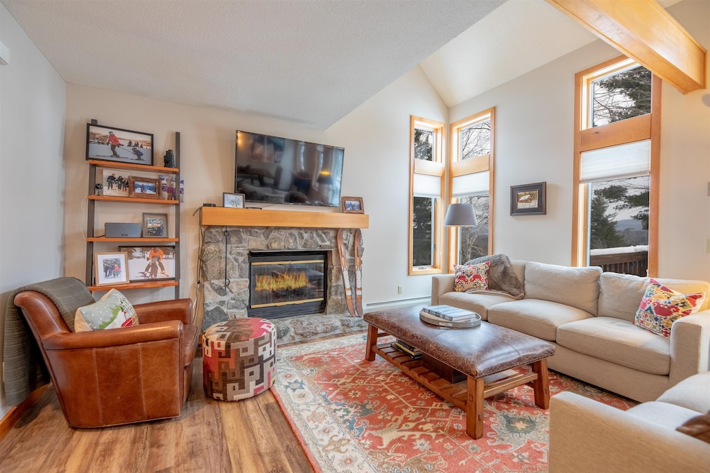 living room featuring wood-type flooring, a stone fireplace, vaulted ceiling, and a baseboard heating unit