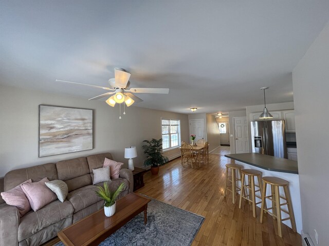 living room with ceiling fan, a baseboard heating unit, and light wood-type flooring