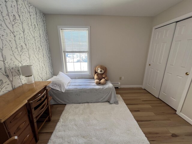 bedroom with a baseboard radiator, light hardwood / wood-style floors, and a closet