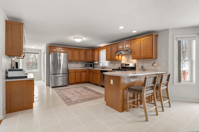 kitchen with backsplash, a kitchen bar, kitchen peninsula, stainless steel appliances, and plenty of natural light