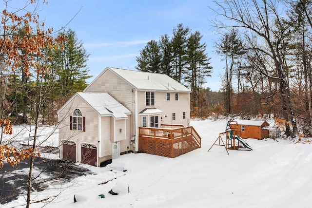 snow covered back of property featuring a garage, a playground, and a deck