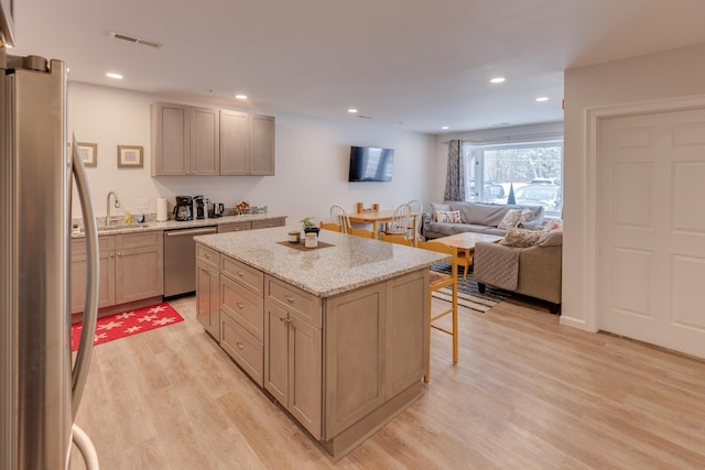 kitchen with appliances with stainless steel finishes, a kitchen breakfast bar, a center island, light stone countertops, and light wood-type flooring