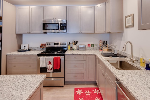 kitchen with sink, light wood-type flooring, gray cabinets, stainless steel appliances, and light stone countertops