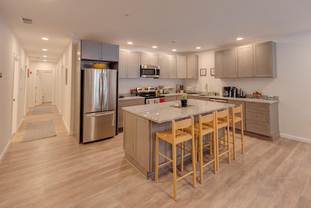 kitchen with a kitchen bar, a center island, light wood-type flooring, stainless steel appliances, and light stone countertops