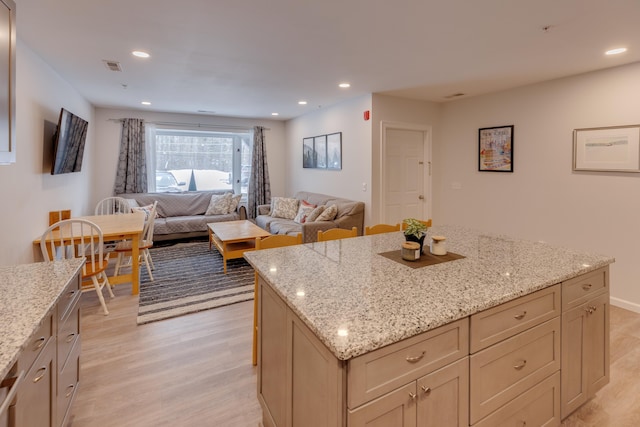 kitchen with a kitchen island, light stone countertops, and light wood-type flooring