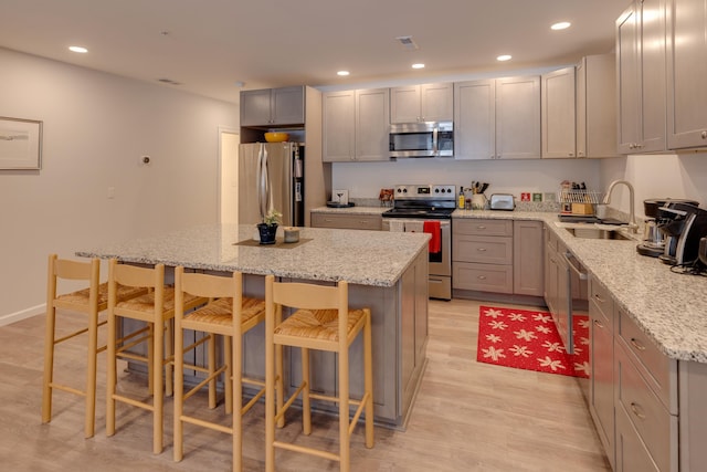 kitchen with a kitchen island, light stone countertops, appliances with stainless steel finishes, and sink