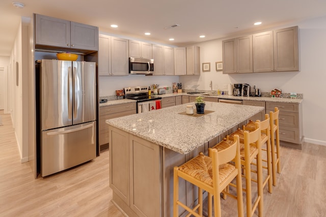 kitchen featuring a breakfast bar, light stone counters, a center island, gray cabinets, and stainless steel appliances