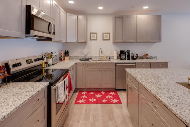 kitchen with appliances with stainless steel finishes, sink, light stone counters, and light hardwood / wood-style floors