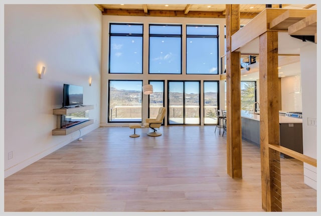 unfurnished living room with beam ceiling, light hardwood / wood-style flooring, and a high ceiling