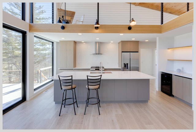 kitchen featuring decorative light fixtures, a spacious island, sink, stainless steel fridge, and wall chimney exhaust hood