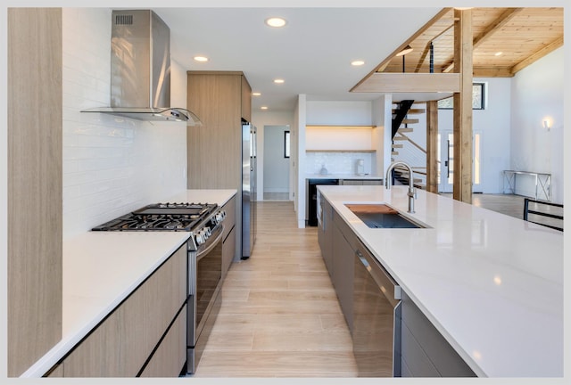 kitchen featuring gray cabinets, appliances with stainless steel finishes, sink, and wall chimney range hood