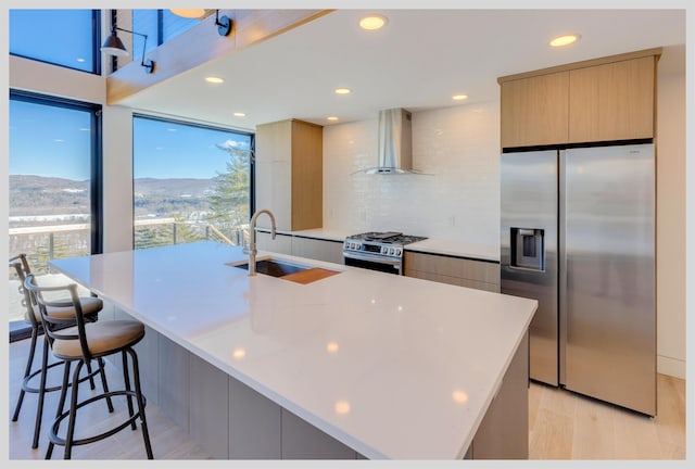 kitchen with sink, a breakfast bar area, stainless steel appliances, wall chimney exhaust hood, and a large island with sink