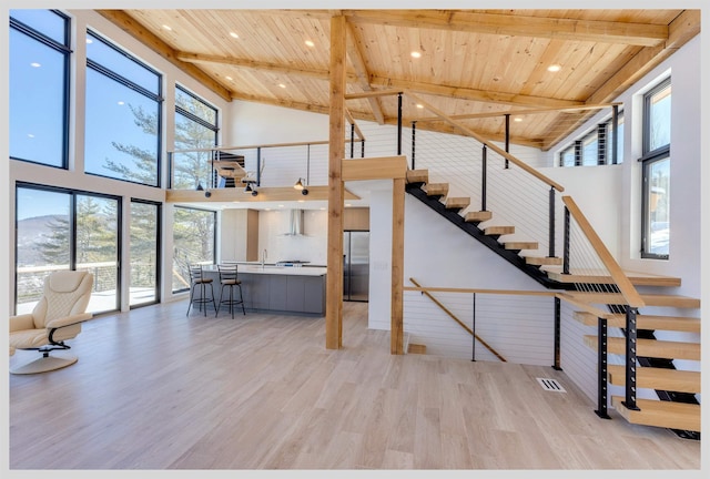 unfurnished living room with sink, wood ceiling, light wood-type flooring, beamed ceiling, and a high ceiling