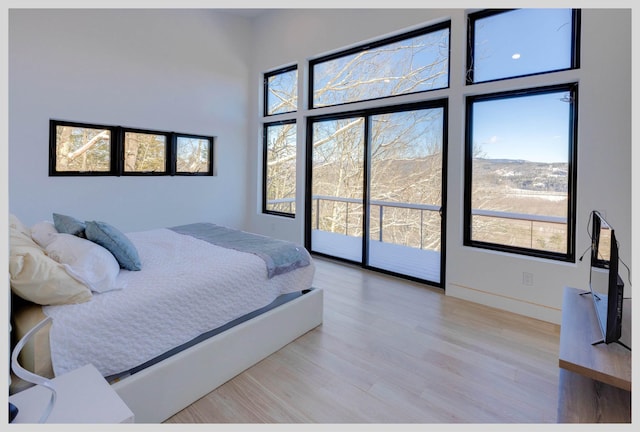 bedroom featuring access to exterior, a high ceiling, and light wood-type flooring