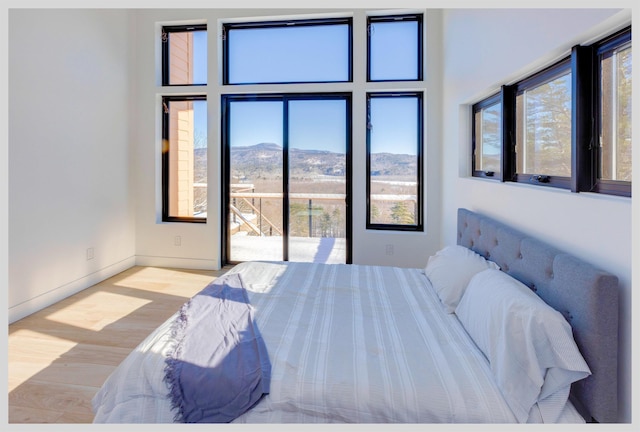 bedroom featuring a mountain view, light hardwood / wood-style floors, multiple windows, and access to outside