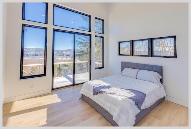 bedroom with light wood-type flooring, a high ceiling, and access to outside