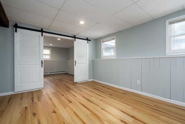 spare room featuring a baseboard heating unit, plenty of natural light, light hardwood / wood-style floors, and a barn door