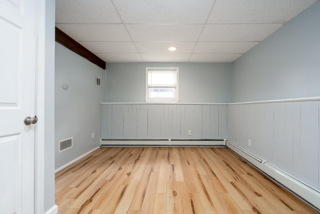 empty room with a drop ceiling, a baseboard radiator, and light hardwood / wood-style floors