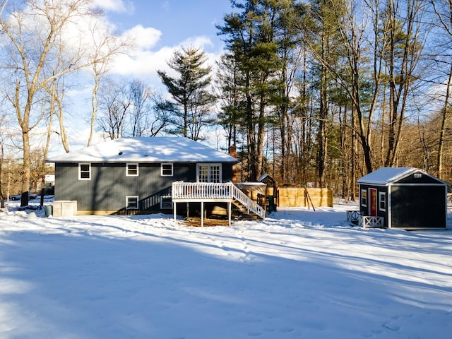 snow covered back of property with an outbuilding and a deck