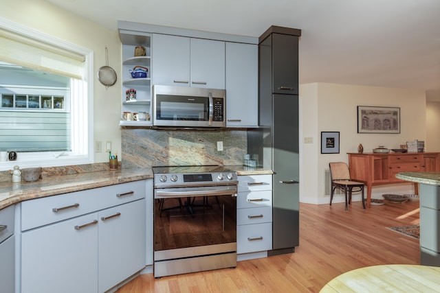 kitchen featuring decorative backsplash, stainless steel appliances, light stone countertops, and light hardwood / wood-style flooring