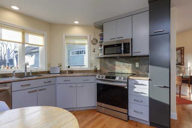 kitchen with sink, tasteful backsplash, light wood-type flooring, dark stone counters, and stainless steel appliances