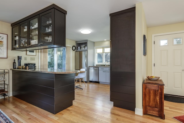 bar with stone counters, appliances with stainless steel finishes, sink, and light hardwood / wood-style flooring