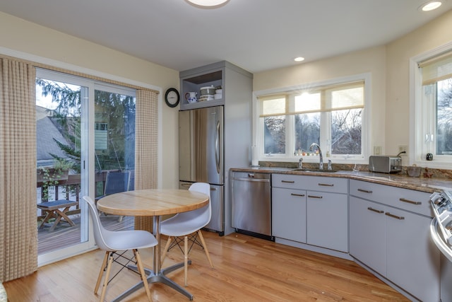 kitchen with appliances with stainless steel finishes, sink, white cabinets, dark stone counters, and light hardwood / wood-style flooring