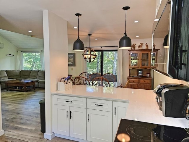 kitchen featuring light hardwood / wood-style floors, white cabinets, cooktop, decorative light fixtures, and kitchen peninsula