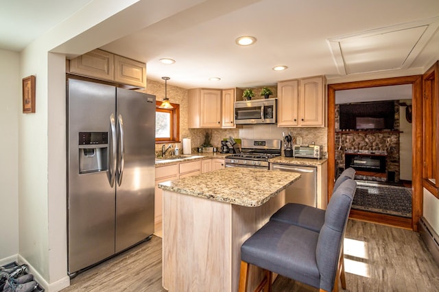 kitchen featuring hanging light fixtures, light wood-type flooring, light brown cabinets, appliances with stainless steel finishes, and a kitchen island