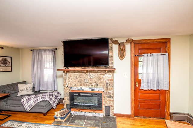 living room featuring wood-type flooring, a stone fireplace, and baseboard heating