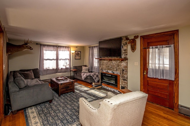 living room featuring wood-type flooring, a stone fireplace, and baseboard heating