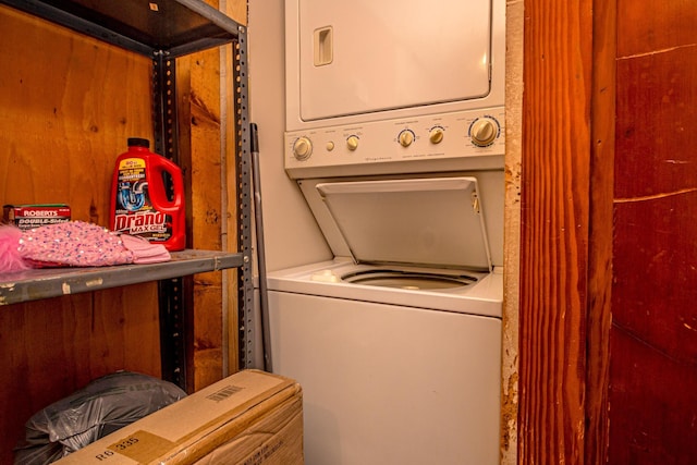 clothes washing area featuring stacked washer / drying machine and wooden walls